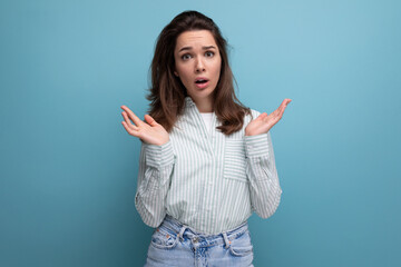 upset young brunette female adult in striped shirt and jeans on studio background