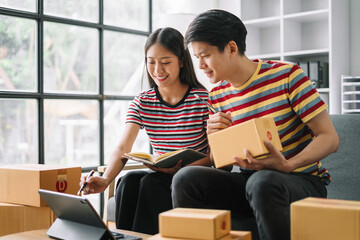 Fototapeta premium couple start up small business owner writing address on cardboard box at workplace.small business entrepreneur SME or freelance asian couple working with box at home.