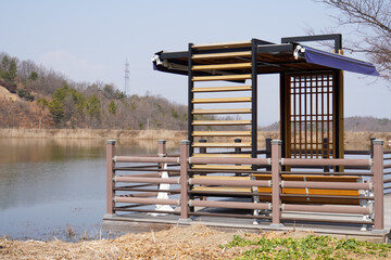  Lakeside pavilion with wooden and metal elements, offering a resting spot with scenic views of the...