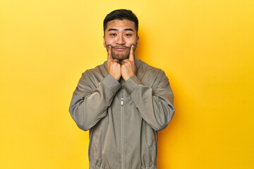 Fototapeta premium Stylish Asian man in gray jacket on yellow studio doubting between two options.