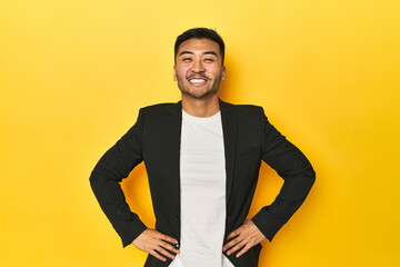 Asian man in black business jacket on yellow studio confident keeping hands on hips.