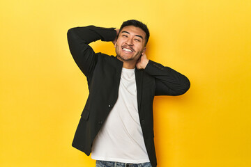Asian man in black business jacket on yellow studio stretching arms, relaxed position.