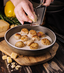 woman grating parmesan on meatballs in cream sauce