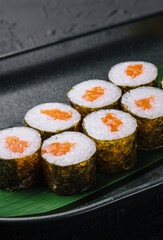 Row of fresh maki sushi rolls on black plate