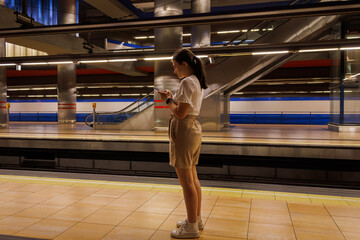 teenage girl in shorts looking at her cell phone in the subway station to know her destination