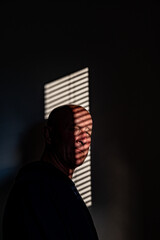 A portrait of a middle aged man against projected window blnds on a wall.