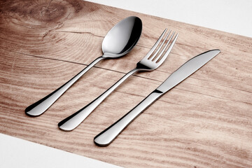 Blank cutlery laying on a fake piece of wood, on a white table.