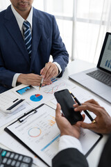 Business team and two colleagues discussing data from graph Financial charts and documents use mobile phones to contact negotiations. Planning on the office desk, startup business concept.