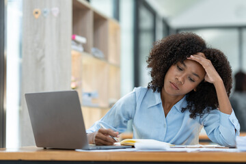 Obraz premium Young American businesswoman working on the laptop with documents and stressing at work from working on financial documents in office Overworked woman concept.
