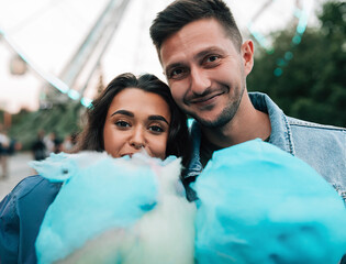 Portrait of a young couple looking at the camera holding a blue cotton candy