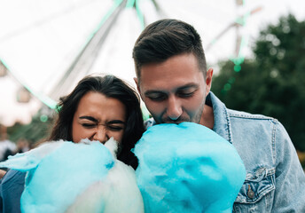 Close-up of a young couple biting blue cotton candy in an amusement park