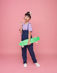 Full length happy asian children girl holding skateboard on pink studio background. People lifestyle relax