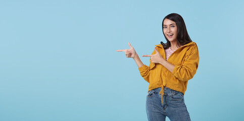 Happy young Asian teen woman standing with her pointing finger aside isolated on blue background with copy space.
