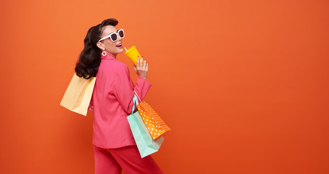 Cheerful happy fashionable woman enjoying shopping, she is carrying shopping bags isolated on orange copy space background.