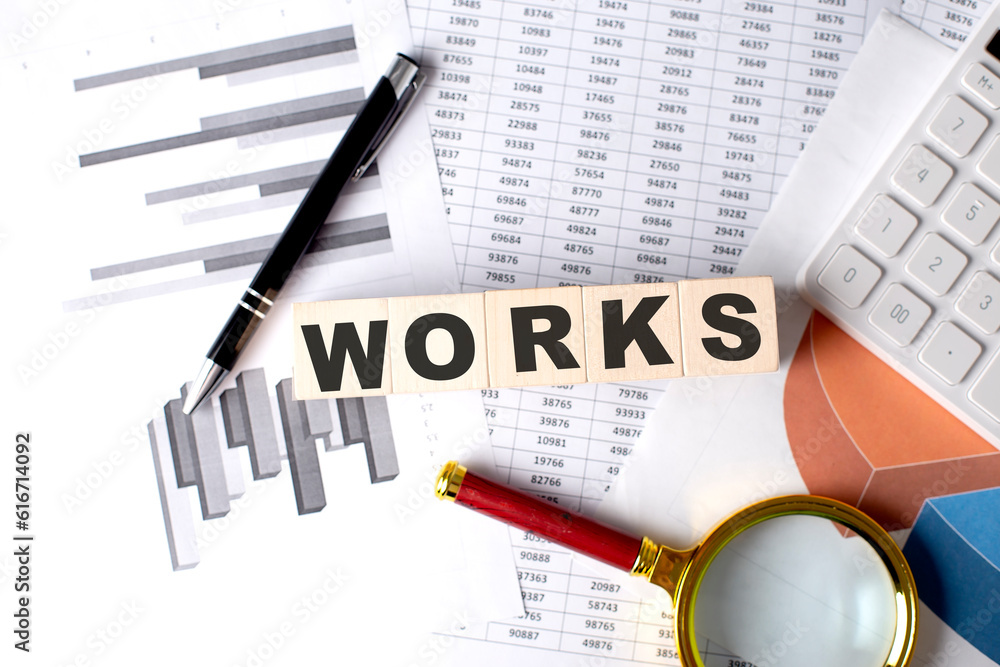 Poster works text on wooden block on graph background with pen and magnifier
