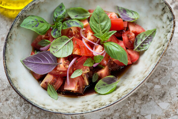 Closeup of tomato salad with balsamic sauce and fresh basil leaves in a grey bowl, horizontal shot, selective focus