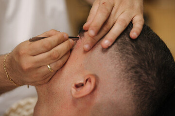 Close-up of barber man trimming eyebrows with tweezers for confident man