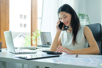 Smiling female entrepreneur sitting at bright modern office and talking on mobile phone.