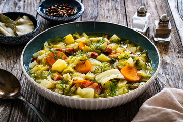 Hot cabbage soup with bacon on wooden table
