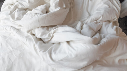 Selective focus of disheveled and wrinkled white soft linen blanket on the bed.