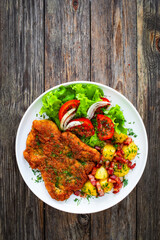 Breaded fried pork chop with fresh vegetable salad and potatoes on wooden table
