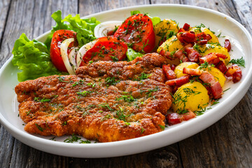 Breaded fried pork chop with fresh vegetable salad and potatoes on wooden table
