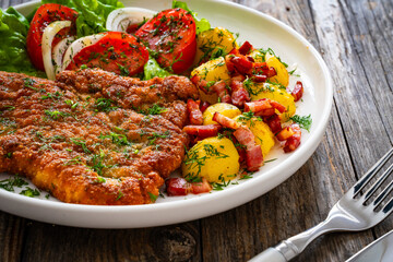 Breaded fried pork chop with fresh vegetable salad and potatoes on wooden table
