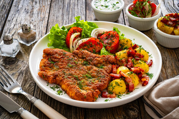 Breaded fried pork chop with fresh vegetable salad and potatoes on wooden table
