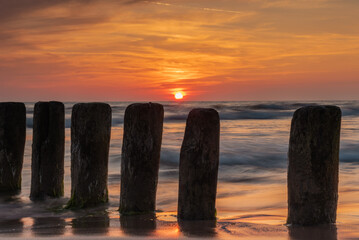 Sunset on Baltic sea shore with old wooden breakwater poles sticking out of the sea in Bernati, Latvia. Long exposure photography.