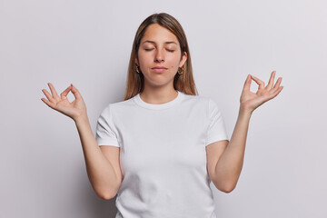Peaceful woman immerses herself in moment of mindfulness practicing meditation with closed eyes and fingers forming yoga sign wears casual t shirt isolated over white background finding inner peace