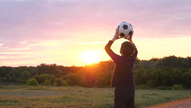A kid plays ball in the park at sunset. The boy dreams of becoming an athlete. The child throws the ball up. kids dreams