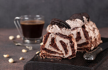 Sliced chocolate meringue roll with cookies on a wooden board and cup of coffee on dark gray...