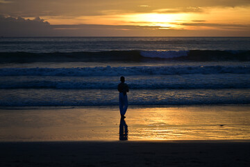 Fototapeta premium A man walks at the beach of Phuket-Thailand in the sunset while he looks at his smartphone.