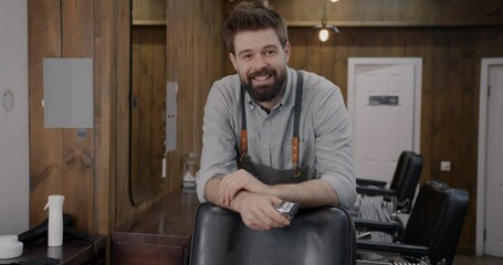 Portrait of skilled male barber standing in studio holding shaving machine smiling looking at camera. Profession and barbershop concept.