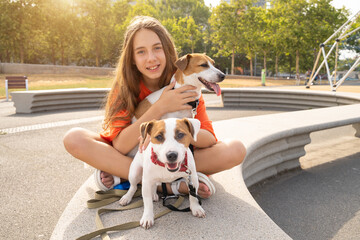Two dogs and long haired teenager girl sitting in the park happy smiling. hugging cuddling, petting two pets small white Jack Russell terriers friends, Summer in big city. Pets love and trust
