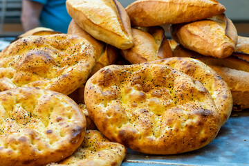 Ramazan pidesi, Turkish flatbread baked during the month of ramadan is a round bread with fennel and sesame seeds on top. It has unique texture and taste. A woman is slicing it on wooden board. - obrazy, fototapety, plakaty