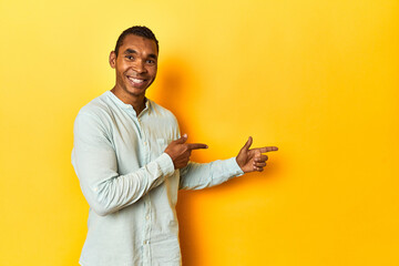 African American man in blue shirt, yellow studio, excited pointing with forefingers away.