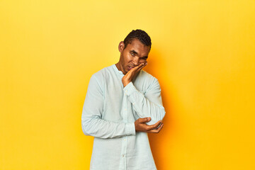 African American man in blue shirt, yellow studio, who is bored, fatigued and need a relax day.