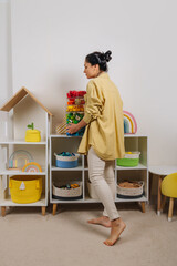 Young woman is holding storage boxes toys. Mom sorted by colors children's toys in transparent...