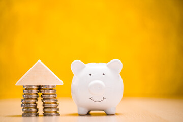 Piggy bank and stack gold coin of the house model with growing interest on the yellow background  in the office, Saving money for buy home or loan for investment of real estate concept.