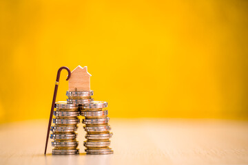Home model put on the stack gold coin with growing interest and walking cane on the yellow background in the office, Saving money for retirement and planning in the future concept.