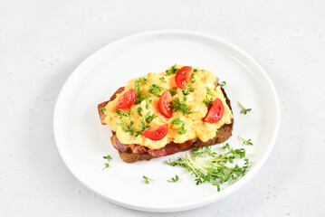 Scrambled eggs with microgreen, bacon and tomato slices on bread