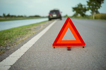  Red emergency stop sign with broken down car on the road waiting to be repaired. Close-up of red emergency stop sign placed on the road for vehicle accidents or breakdowns for road safety.