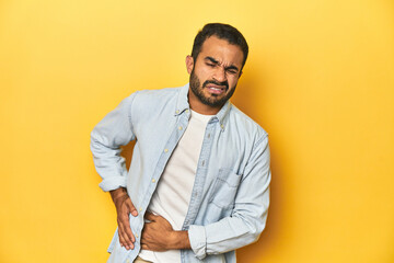 Casual young Latino man against a vibrant yellow studio background, having a liver pain, stomach...