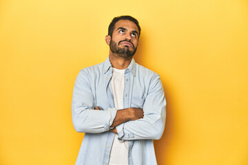 Casual young Latino man against a vibrant yellow studio background, tired of a repetitive task.