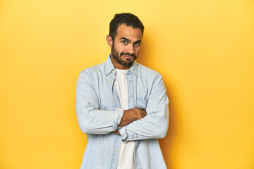 Obraz premium Casual young Latino man against a vibrant yellow studio background, suspicious, uncertain, examining you.