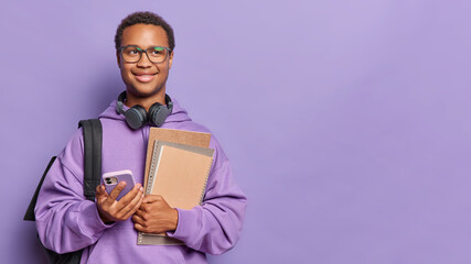 Modern student poses with textbooks and smartphone has dreamy expression returns after classes in...