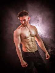 Handsome male bodybuilder in studio shot, looking down to a side