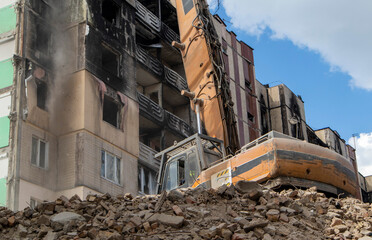 Facade of a residential abandoned multi-storey building after a strong fire. A construction excavator with a hydraulic crusher demolishes a house for repairs. The collapse of a residential building.