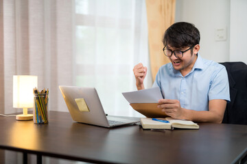 Asian handsome man reading acceptance letter for job application who pass the qualifying exam with joy and success at their home desk.